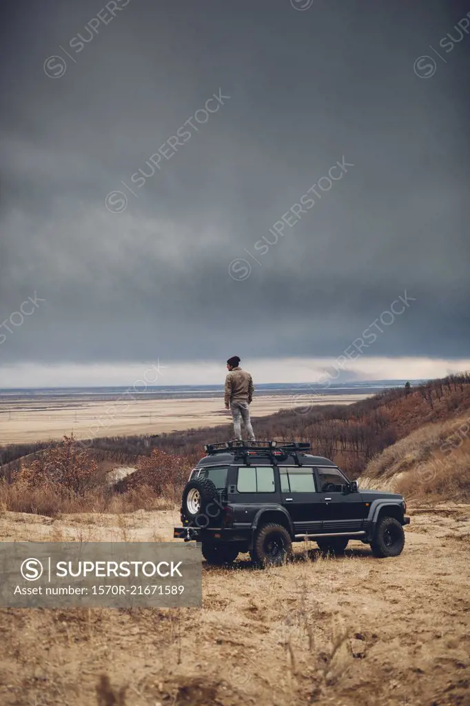 Distant man standing on top of sports utility vehicle over land against cloudy sky, Amur, Russia