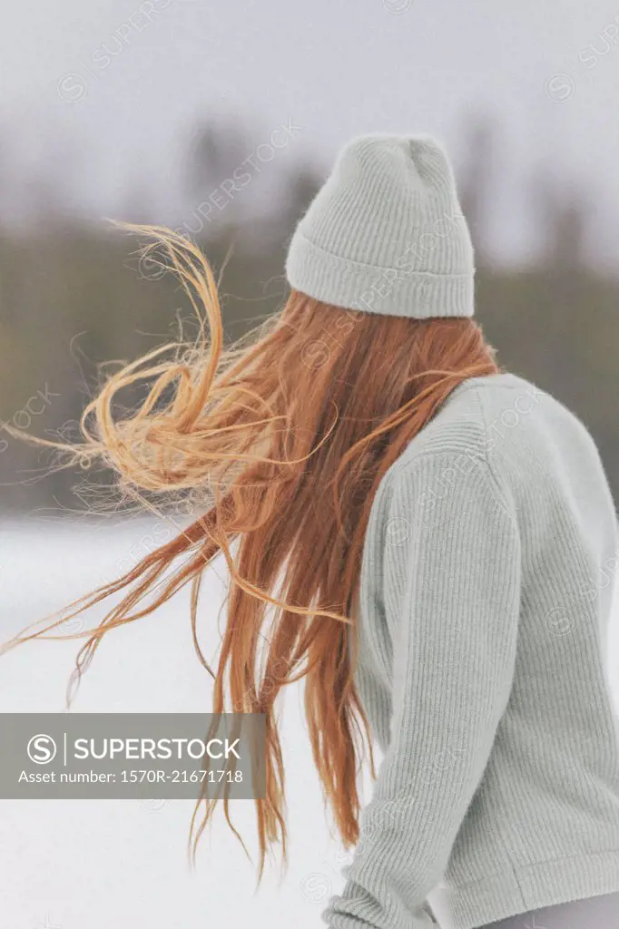 Young woman with long red hair wearing knit hat and sweater against clear sky