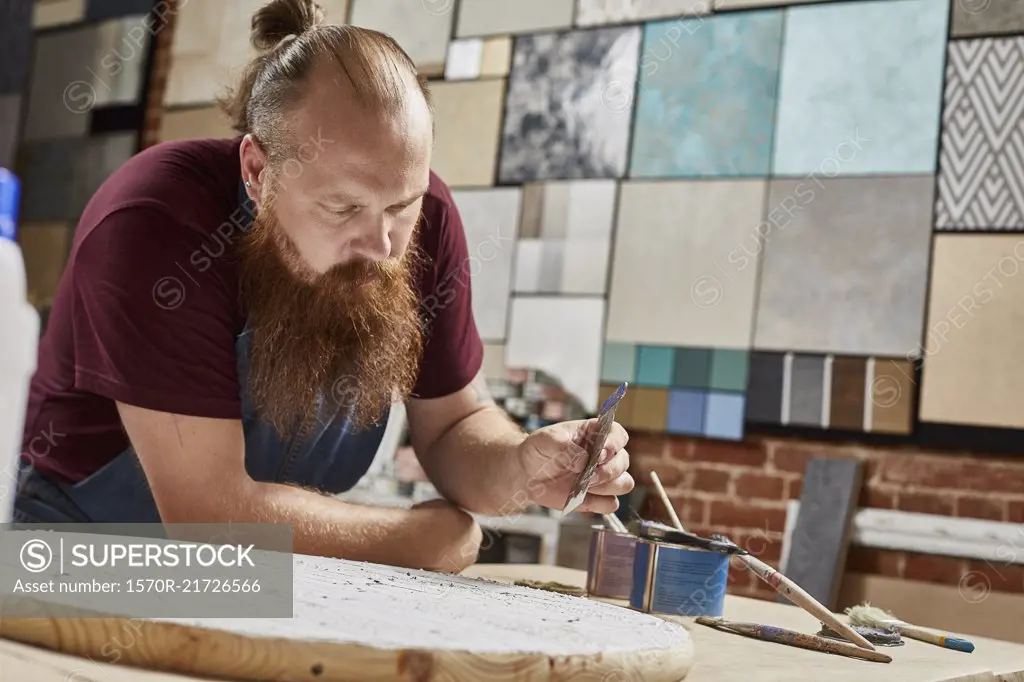 Man holding sand paper while leaning on workbench