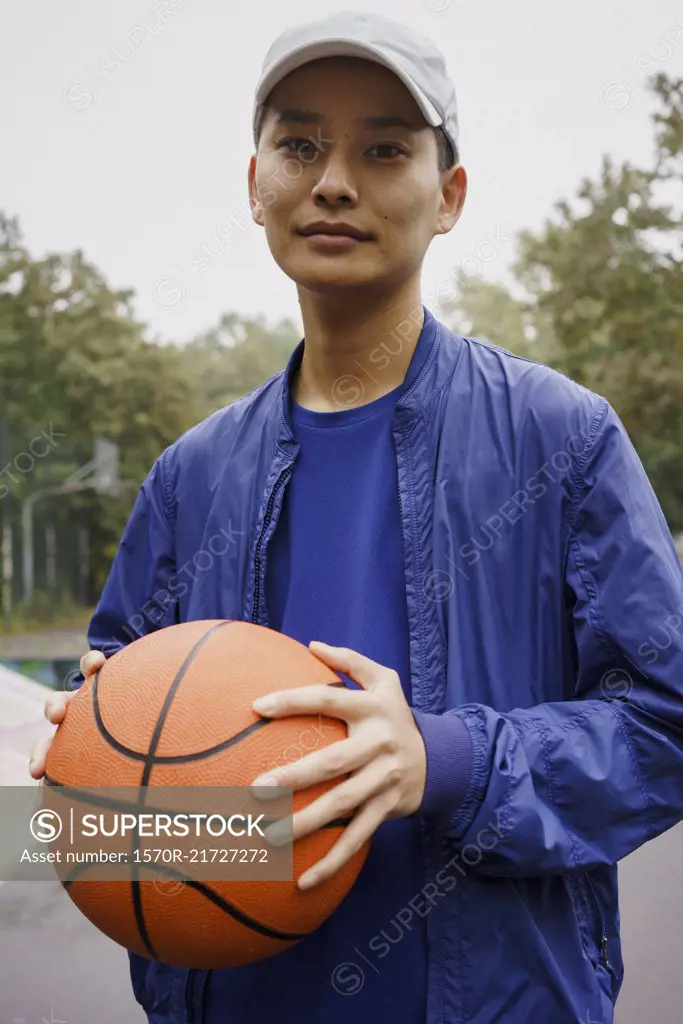 Portrait of young man holding ball while standing at park