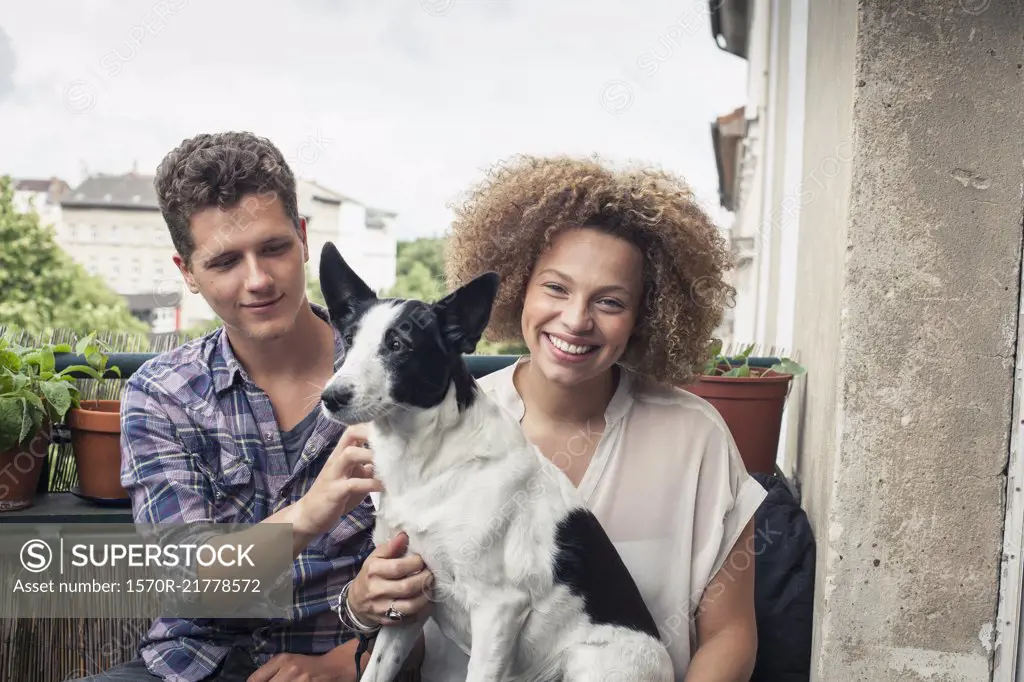 Portrait of smiling woman carrying dog sitting with friend in balcony