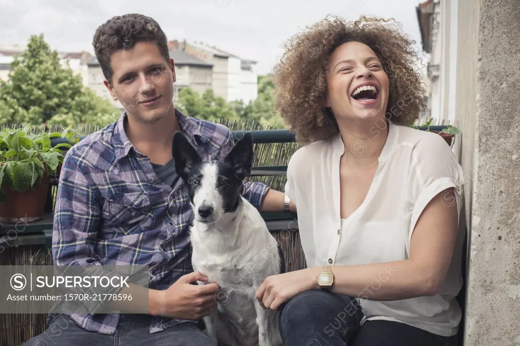 Happy young friends sitting with dog in balcony