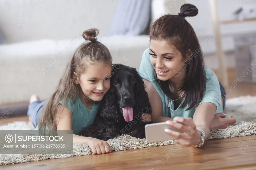 Young woman with daughter and dog taking selfie using smart phone at home