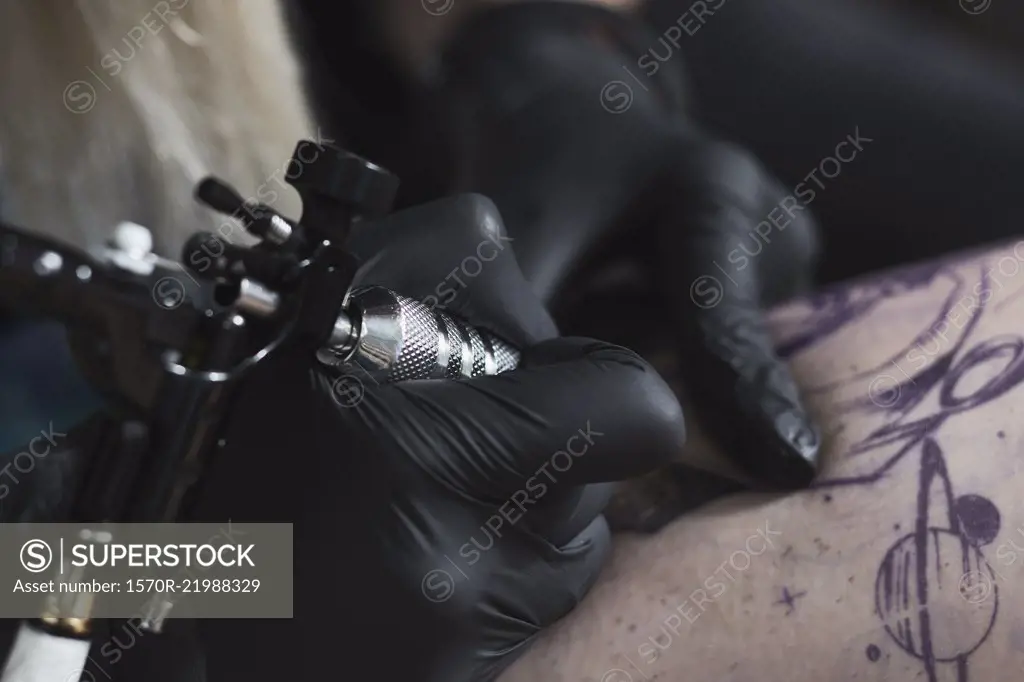 Cropped image of artist wearing gloves tattooing on thigh with machine