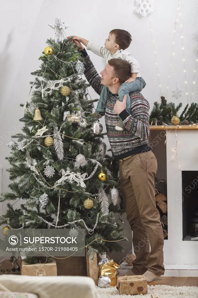 Full length of man carrying son shoulders while decorating Christmas Tree at home