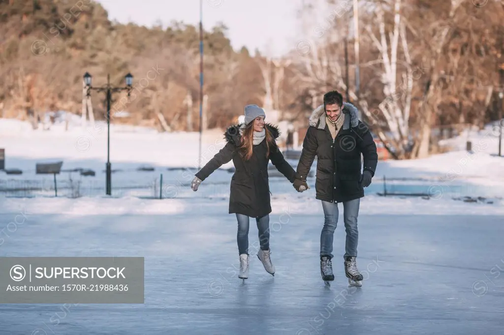 Full length of happy couple holding hands while enjoying ice-skating on rink