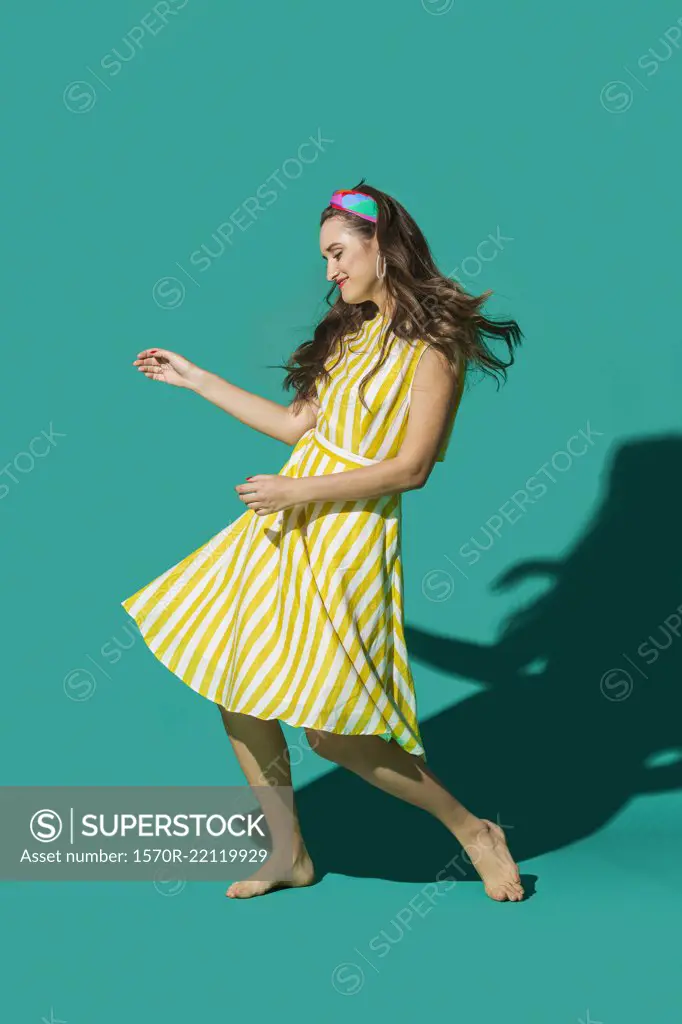 Portrait carefree young woman in striped dress dancing against turquoise background