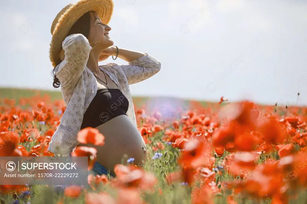 Carefree pregnant woman in sunny, idyllic rural red poppy field