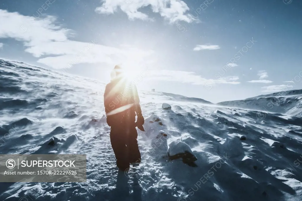 Man walking along sunny snow covered landscape, Reykjadalur, Iceland