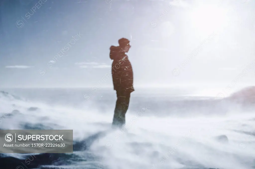 Teenage boy standing on sunny, windy snow covered mountain, Reykjadalur, Iceland