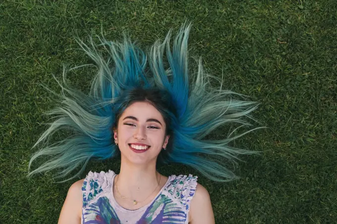 Overhead portrait carefree young woman with blue hair laying in grass