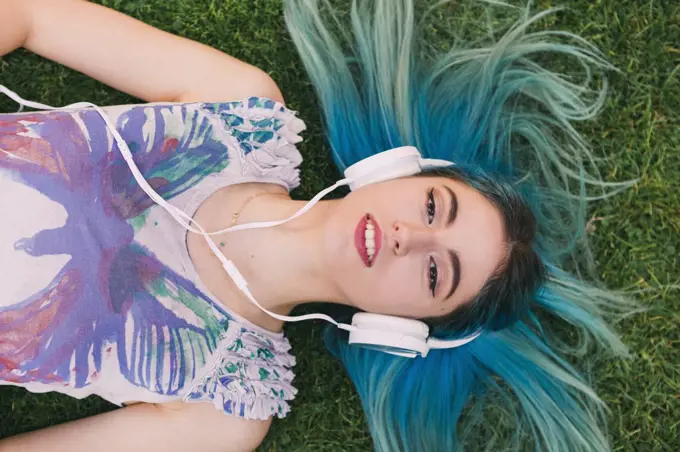 Overhead portrait young woman with blue hair listening to music with headphones