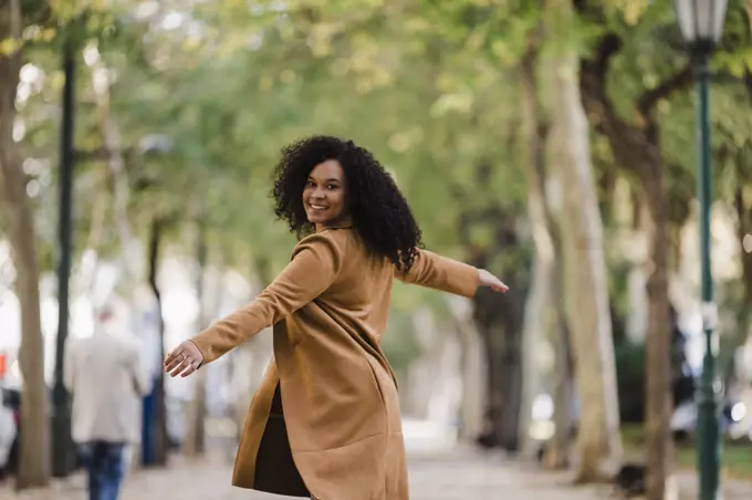 Portrait carefree young woman dancing on treelined sidewalk