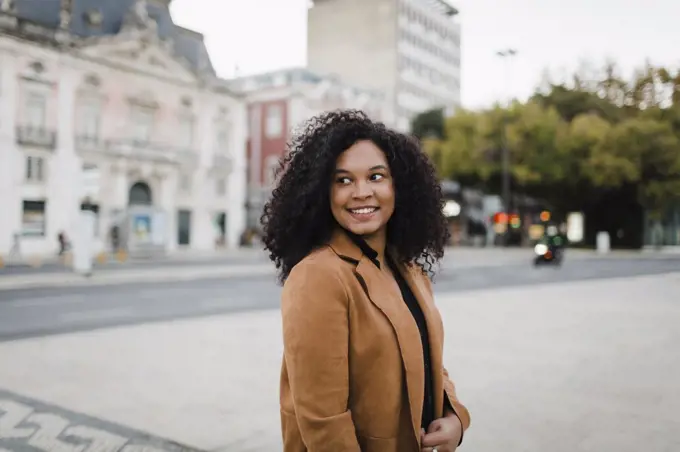 Happy young woman looking over shoulder on urban street