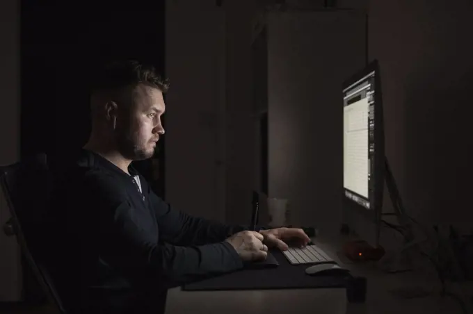 Man with earbuds working late at computer in dark room