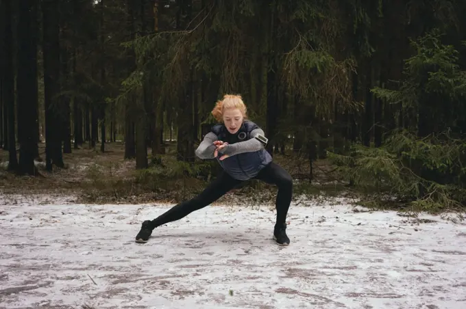 Athletic female runner stretching in snowy woods