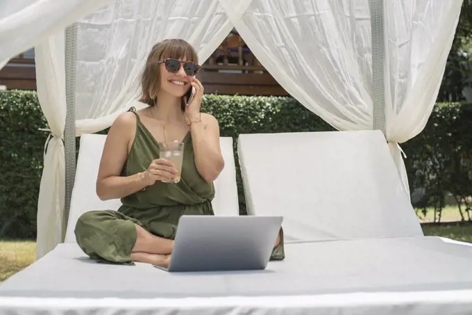 Happy woman talking on smart phone at laptop in cabana
