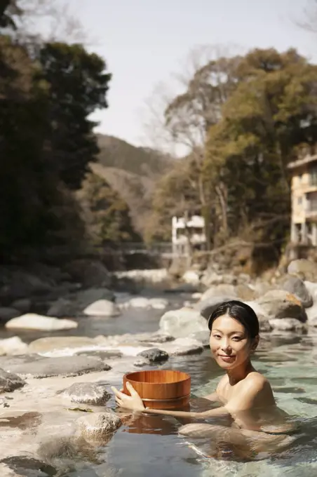 Portrait beautiful young woman with bucket in sunny pool at Onsen