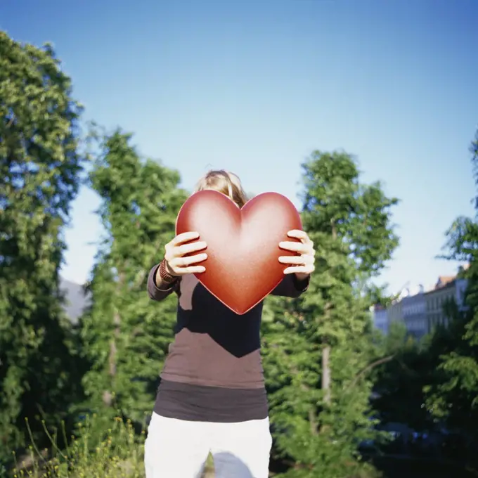 Woman holding a red heart in front of her face