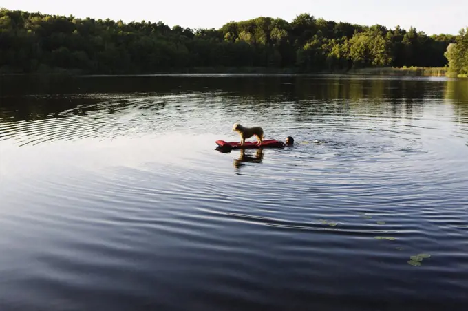 A man pushing a dog on a pool raft in a lake