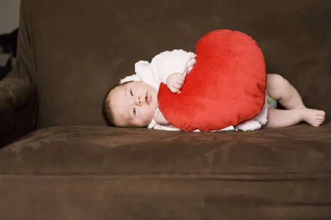 A baby lying on her side embracing a heart shaped pillow