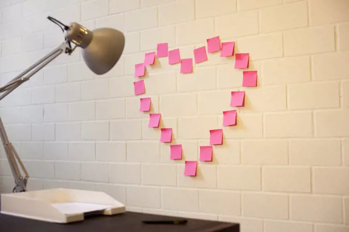 Adhesive notes arranged into the shape of a heart on a wall next to a desk