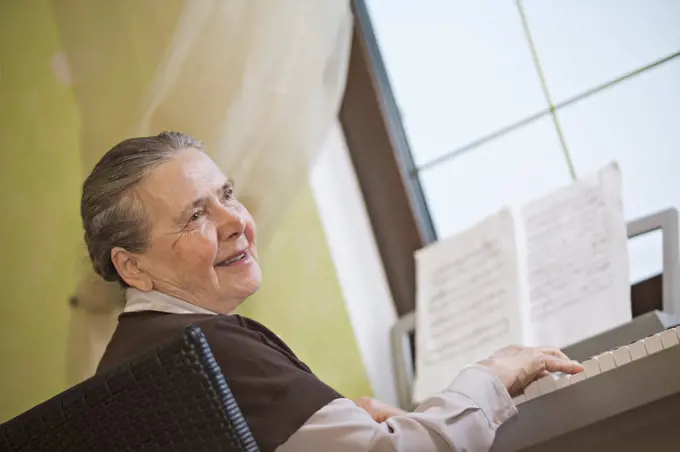 A cheerful senior woman playing an upright piano