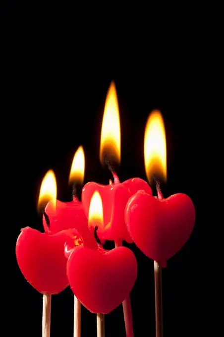 Five lit heart shaped candles on sticks arranged in a group