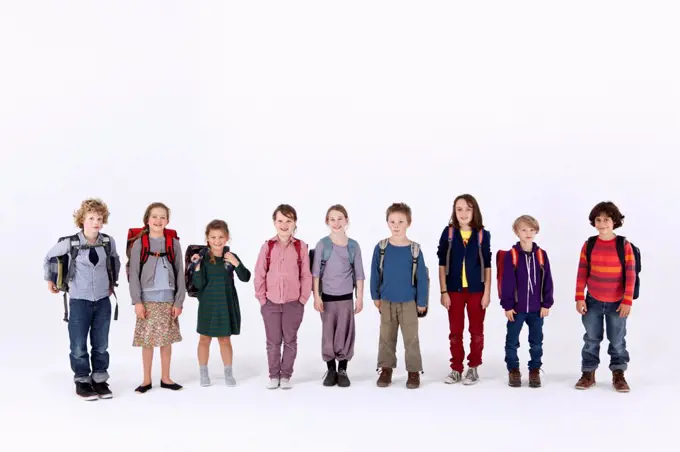 A group of school children wearing backpacks, standing in a row