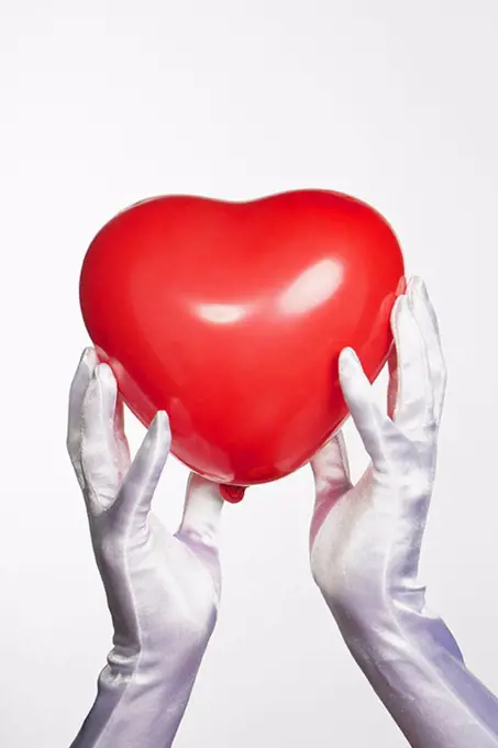 Cropped hands of bride holding heart shape balloon against white background