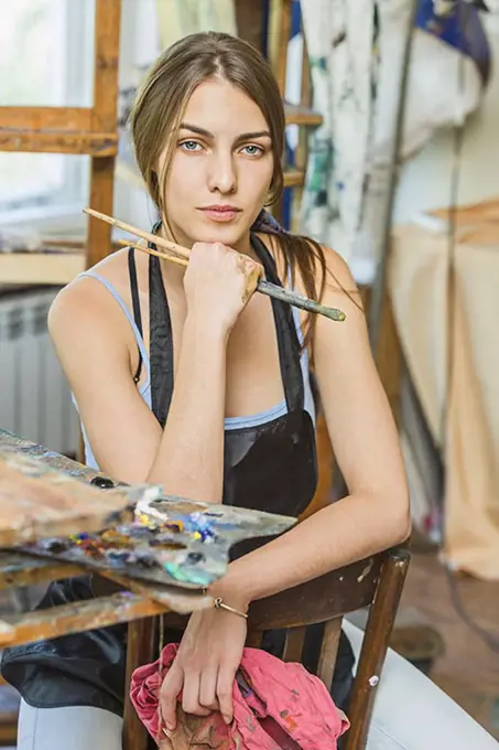 Portrait of beautiful female painter sitting on chair in studio