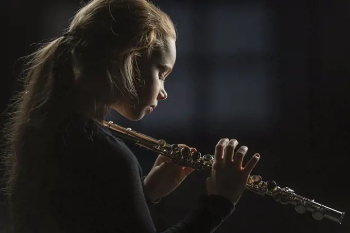 Side view of girl holding flute against black background