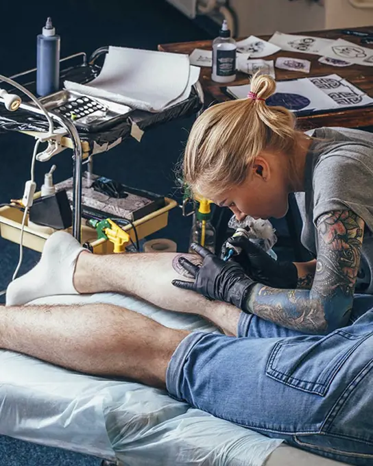 Artist tattooing design on man's leg at studio