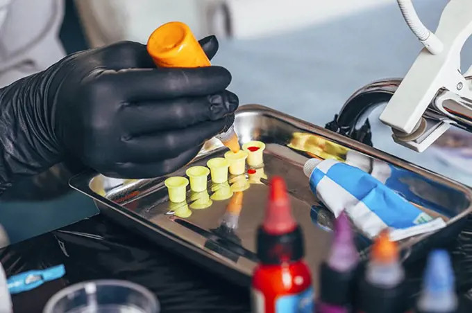 Cropped image of tattoo artist filling ink in containers at art studio