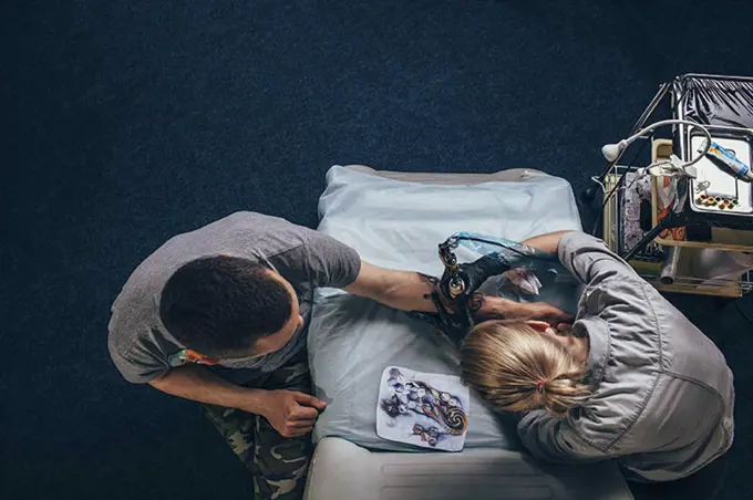 High angle view of tattoo artist tattooing on human hand at studio