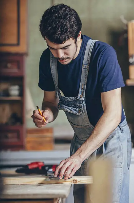 Carpenter marking on wood with pencil and ruler at workshop