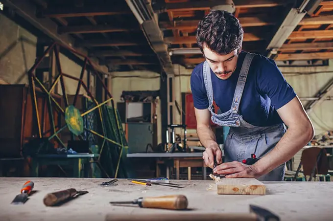 Carpenter using chisel on plank of wood in workshop