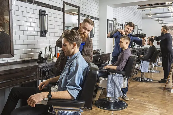 Hairdressers cutting male customer's hair in salon