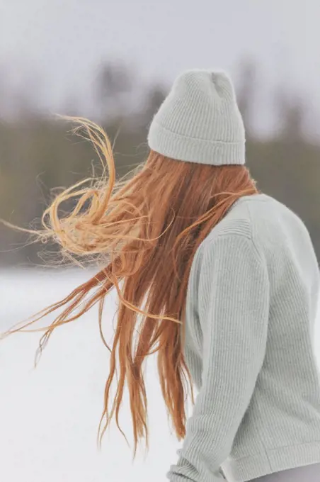 Young woman with long red hair wearing knit hat and sweater against clear sky