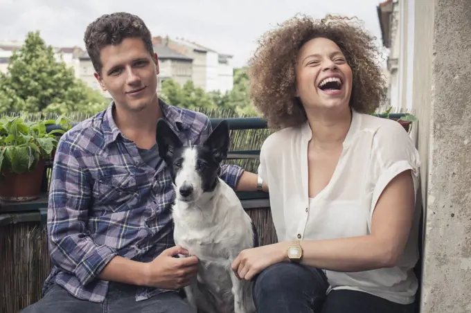 Happy young friends sitting with dog in balcony