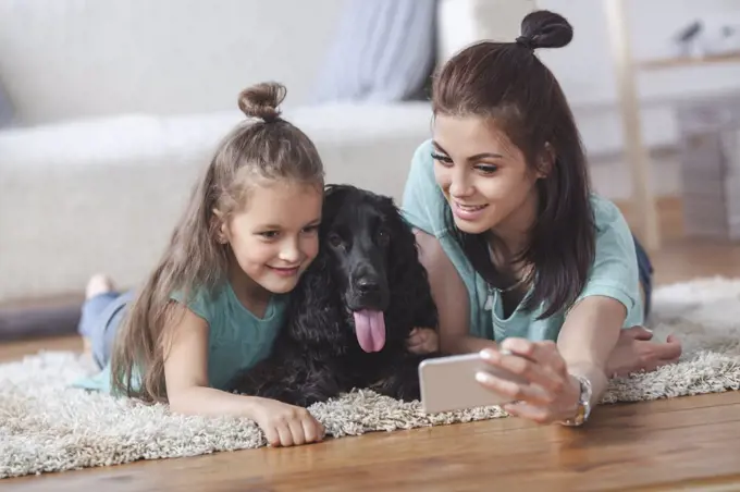 Young woman with daughter and dog taking selfie using smart phone at home