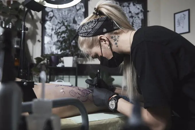 Female artist tattooing on customer's thigh at studio