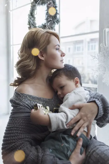 Young woman sitting with son by window at home