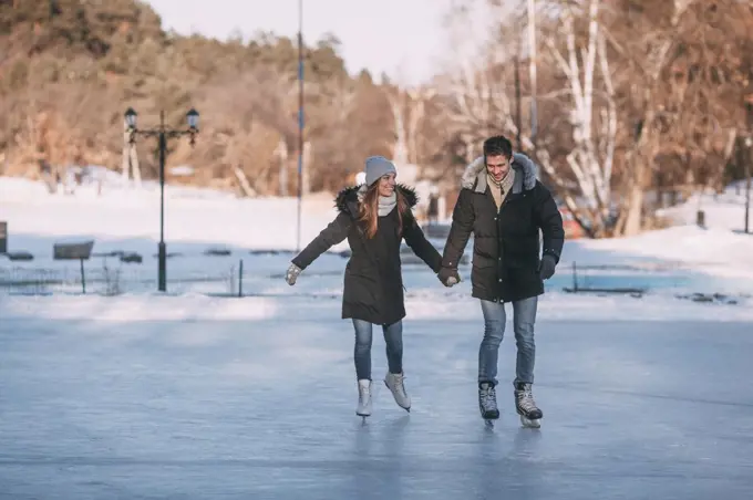 Full length of happy couple holding hands while enjoying ice-skating on rink