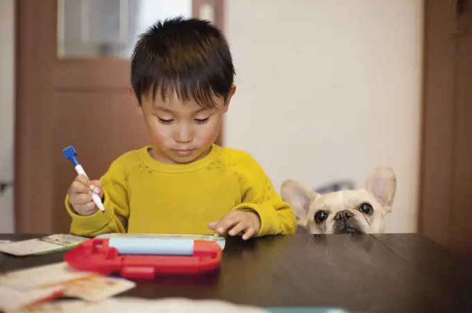 Boy writing on slate while standing by dog at table