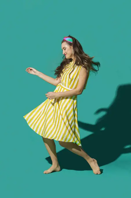 Portrait carefree young woman in striped dress dancing against turquoise background