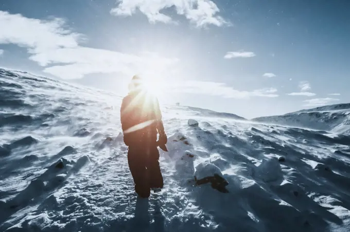 Man walking along sunny snow covered landscape, Reykjadalur, Iceland