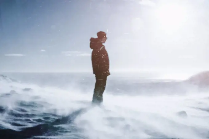 Teenage boy standing on sunny, windy snow covered mountain, Reykjadalur, Iceland