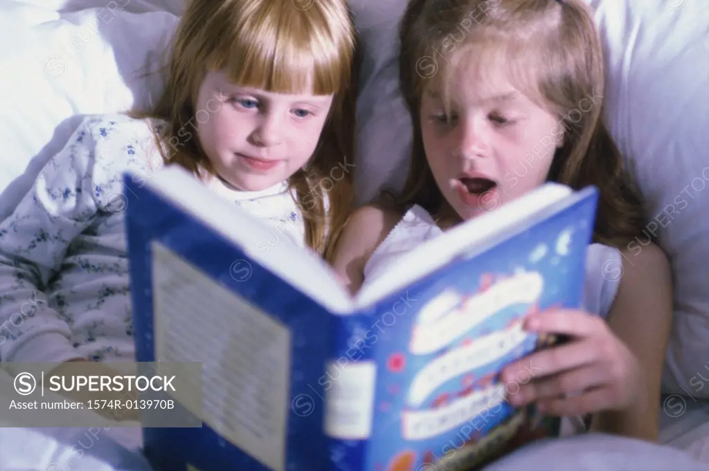 Two girls reading a book in bed