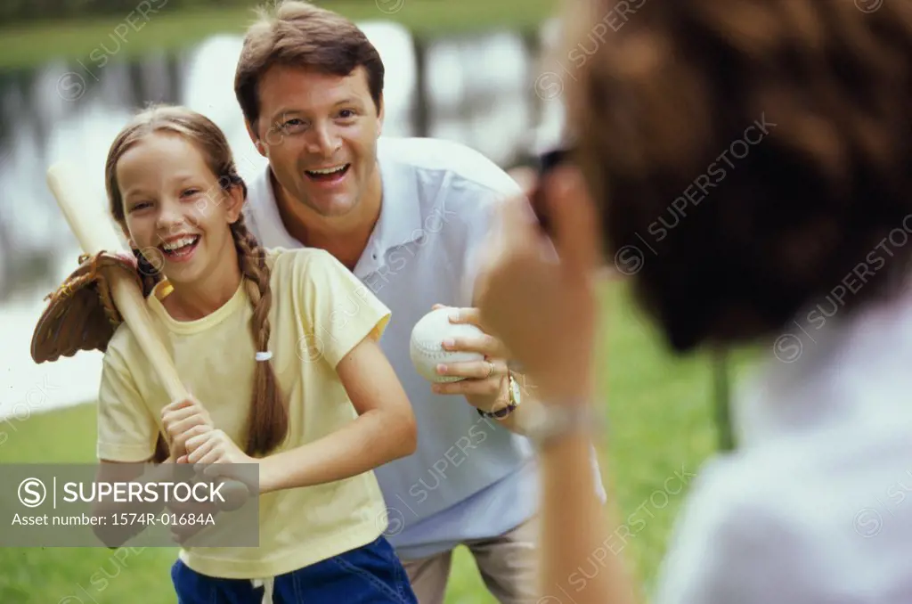 Father and daughter holding baseball equipment in a park